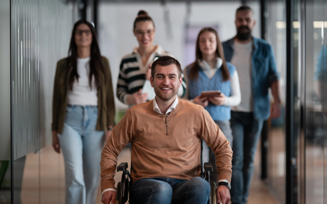 an image of five coworkers, four of which are out of focus in the background, with one individual in a wheelchair in the foreground